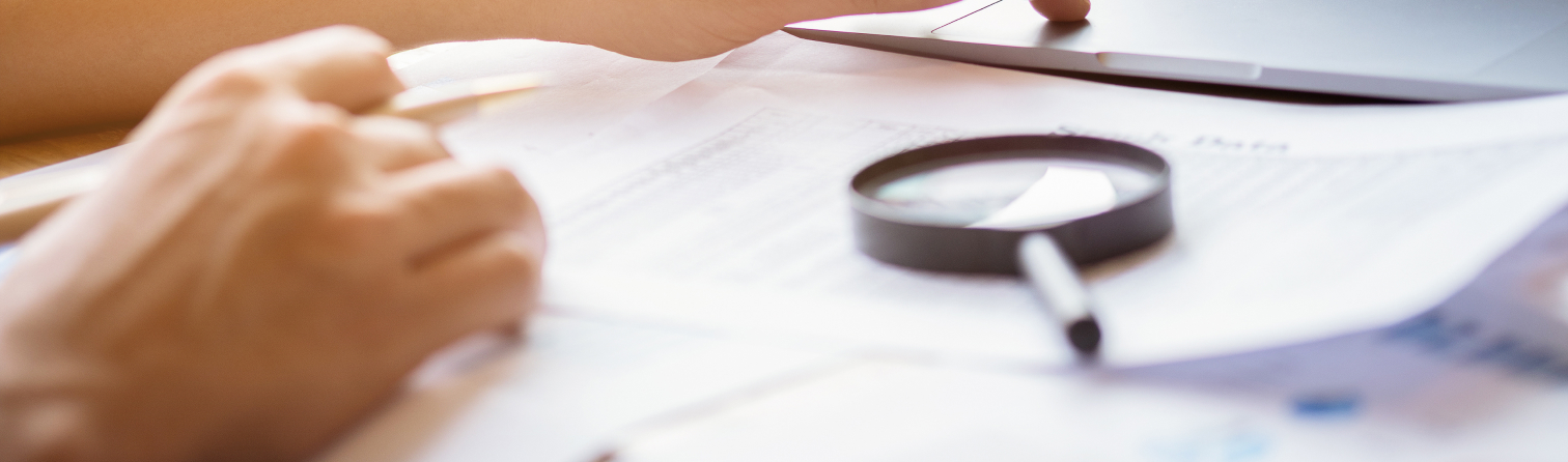 man looking through a magnifying glass to documents